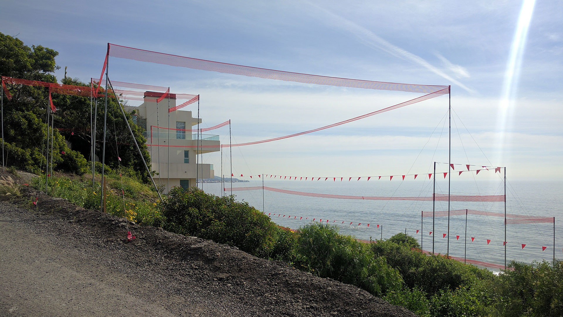 Coastal story pole installation with red mesh netting overlooking the ocean